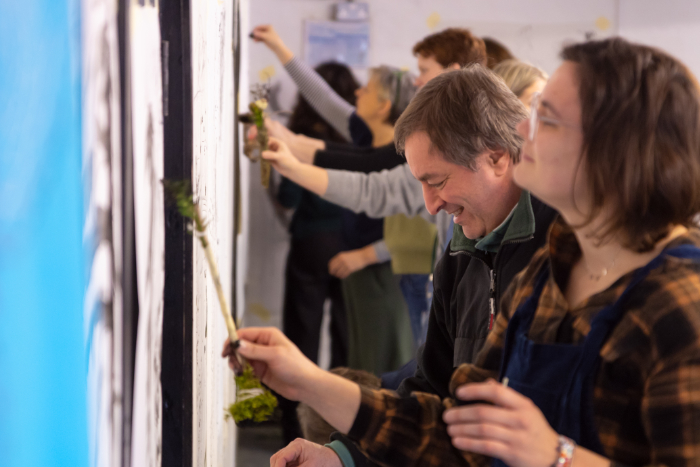 Workshop people drawing with ink on large pieces of paper on the wall. The tools are made with twigs, masking tape, rocks and moss.