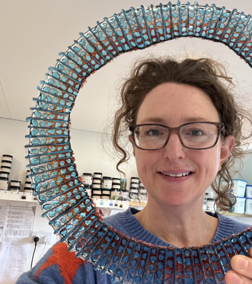 An image of the glass artist Rachael Durkan holding a ring of fused glass in a cellular form.