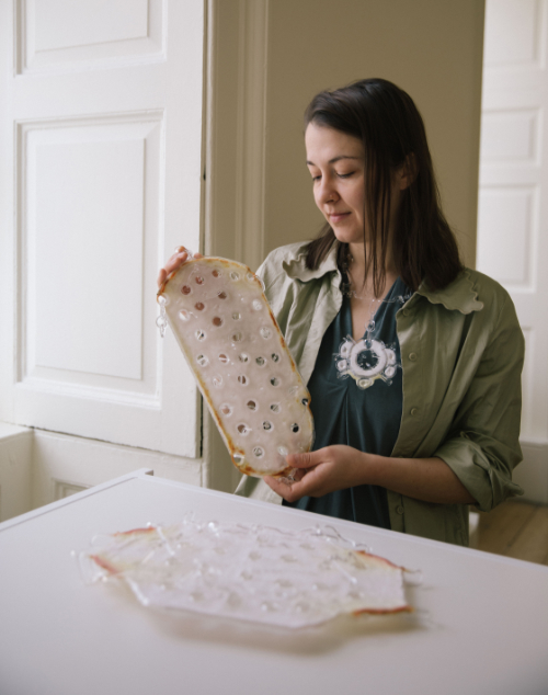 Glass artist Rebecca Tanda wearing a piece of her glass art jewellery and holding a piece of her pate de verre sculpture.