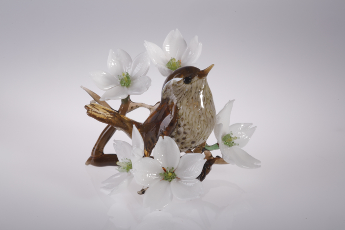 Flameworked glass sculpture of a wren sitting amidst cherry blossom.
