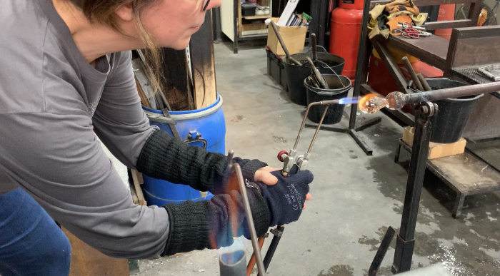 Glass artist Maria Zulueta working with a small torch on a blob of molten glass on a pipe.