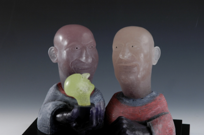 A sculpture in cast glass by David Reekie featuring David Reekie and Mark Holford looking at a smaller glass head.