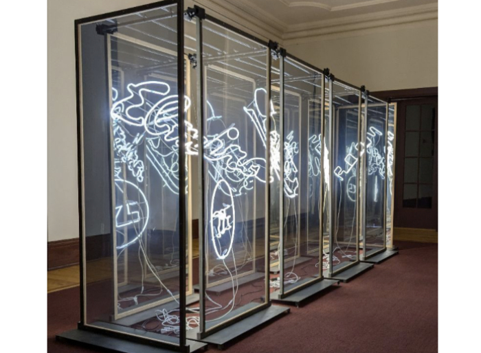 Four large tall glass cabinets standing in a row enclosing illuminated writing. Glass installation by James Ronner.
