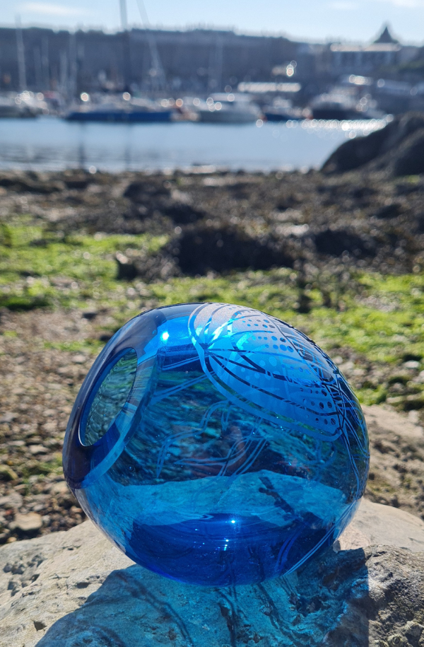 A mid-blue rounded blown glass vessel featuring etched sea creatures.