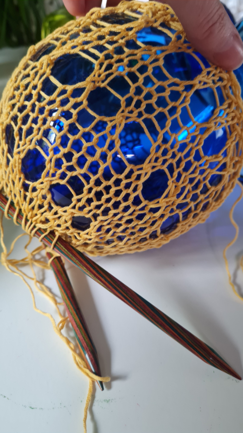 Knitted glasswork in progress. Knitting is created over the surface of a blue glass vessel.