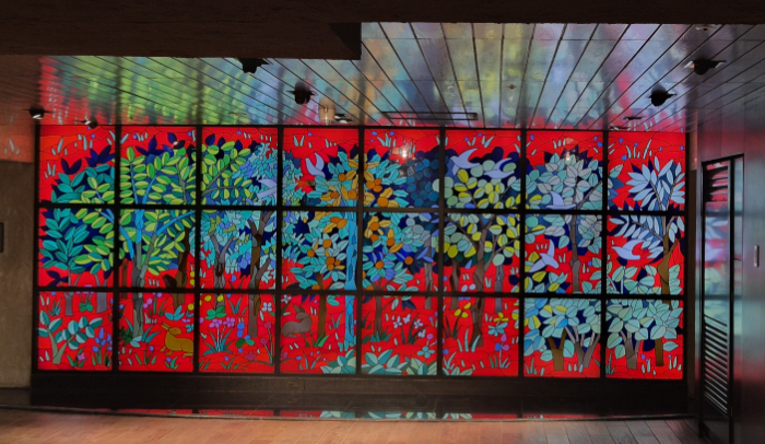 A large, bright and colourful abstracted trees glass panel lit from behind in a Tokyo train station.