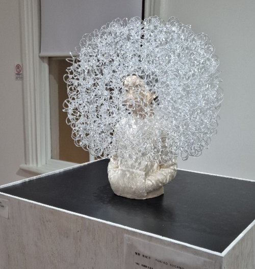 Sculpture of the top half of a girl with swirling clear flame worked glass making a cloud all around her like a dandelion seed head, make by Yukiko Sugano.