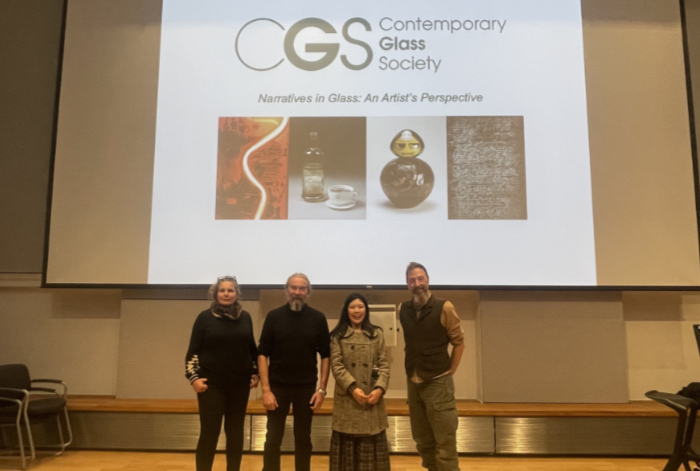 Four speakers standing in front of large overhead screen for their presentations.