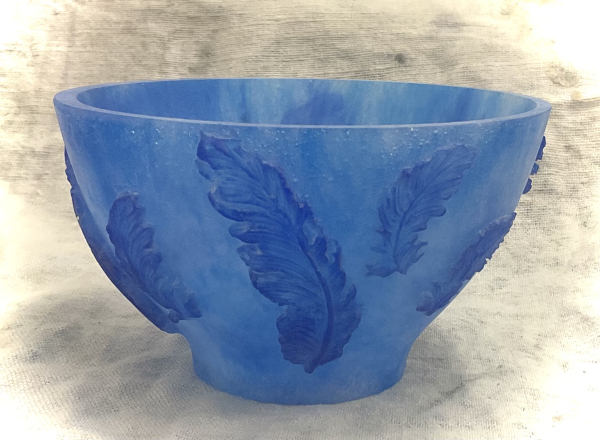 A blue glass bowl featuring darker blue feathers in relief around the outside by Joanna Waddy.