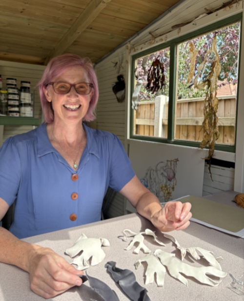 Maria Donnai sitting at her studio desk with porcelain seaweed in front of her.