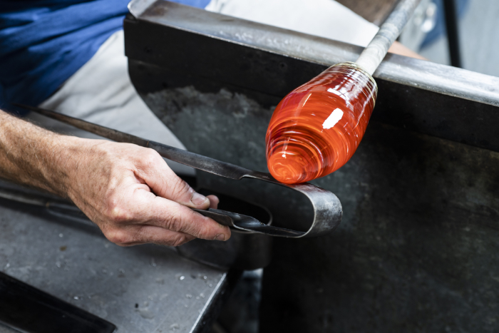 Close up of someone shaping molten glass in the hot shop.
