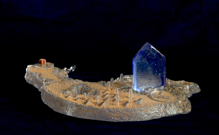Sand-cast glass sculpture of an island floating in space with a house on the top.