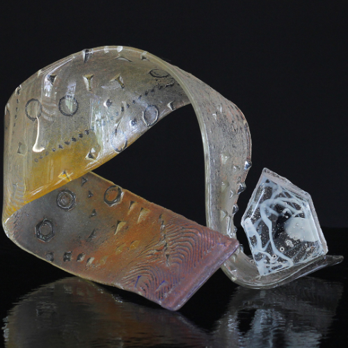 A twisted thin strip of decorated glass with a house shape at the bottom. It represents life as a rollercoaster, but with a safe home base. The glass was removed from the kiln during firing for manipulation.