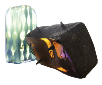 Two brick-like glass pieces in contrast. One is light with an arch shape and tones of wavy green lines running vertically and the other leans horizontally in matt black with splashes of bright colours of orange, yellow and purple, with random spiked areas.