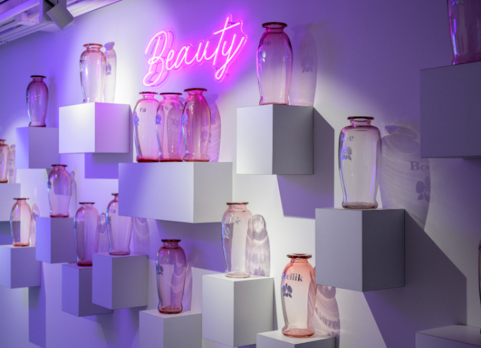 Blown glass vases on cube wall plinths saying the word beauty in 24 languages. Above is a neon sign reading Beauty in pink. By Trish Duggan.
