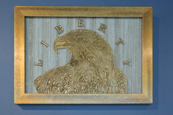 A golden eagle with the word Liberty around it and all framed in a gold frame.