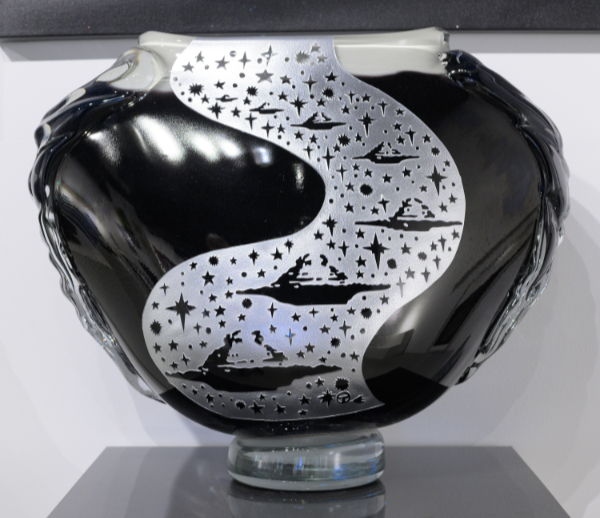 A black rounded glass vase with a design of UFOs ranging from tiny to larger on a wavy white line suggesting they are travelling forward.