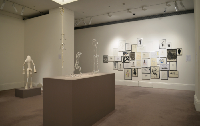 View of exhibition space at Southeby's London including glass figures, a wall of drawings and a gypsum fibre glass figure.