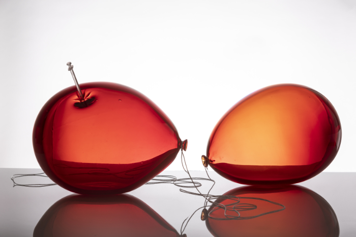 Two red glass balloons, one with a clear glass syringe pressing into its surface. Work is called Till We Meet Again.