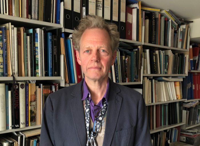 Reino Liefkes of the V&A Museum, London, stands in front of a wall of shelves holding books and folders.