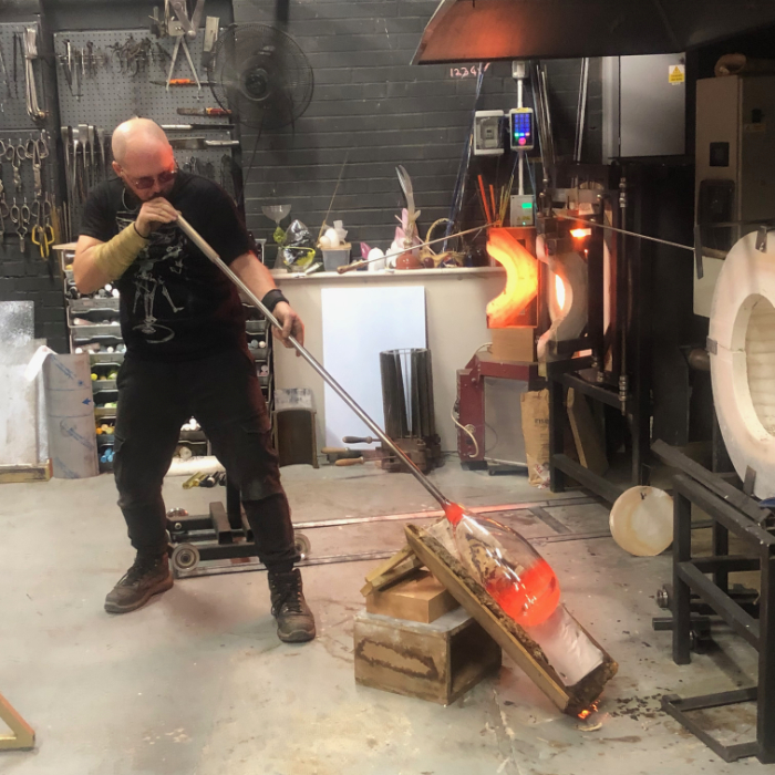 Elliot Walker in the hotshot blowing a cylinder of glass.