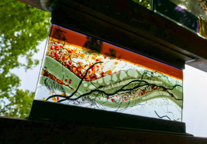 Close-up of fused and mouthblown glass panel featuring greens and oranges with black lines.