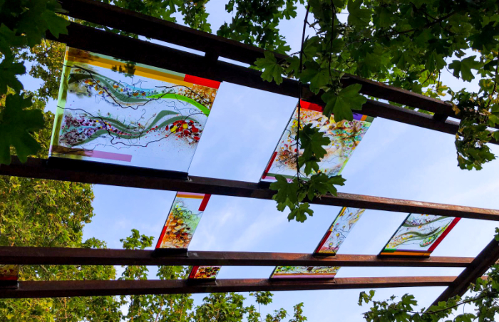 View looking up through rectangular fused and mouthblown glass panels towards the sky with leafy tree branches framing the image.