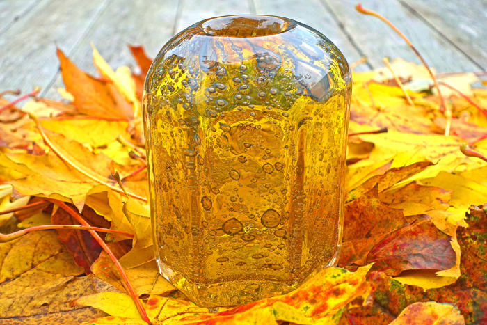 Rich amber dome-topped glass vase featuring honey inclusions presented on a bed of amber coloured autumn leaves.