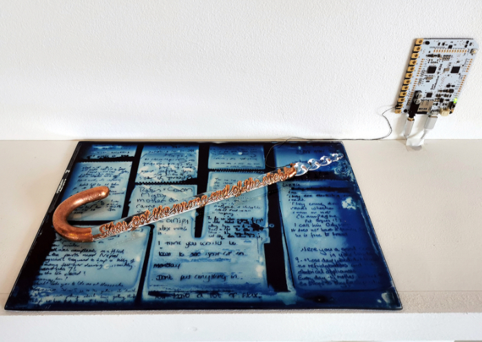 'She's Got the Wrong End of the Stick' artwork features flameworked glass in the form of a long stick with a curved handle like an umbrella handle with the words of the title along the shaft in flameworked glass. It sits on a copper-electroformed, glass cyanotype and has touch-interactive audio.