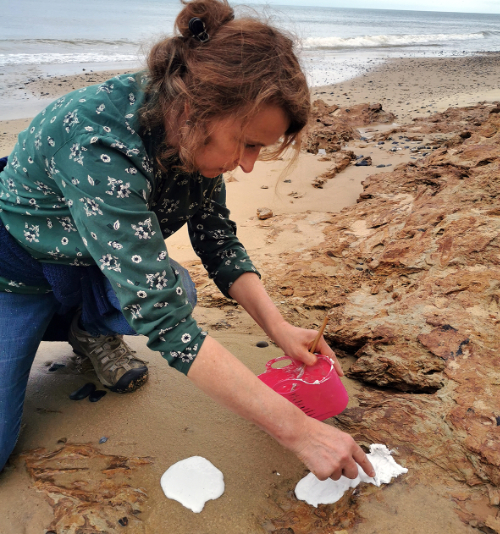 Liz Waugh McManus crouched down on a sandy beach taking textural impressions.