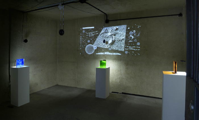 Art installation featuring projected image at the rear with three coloured cast glass slabs on three plinths equidistant in the space.