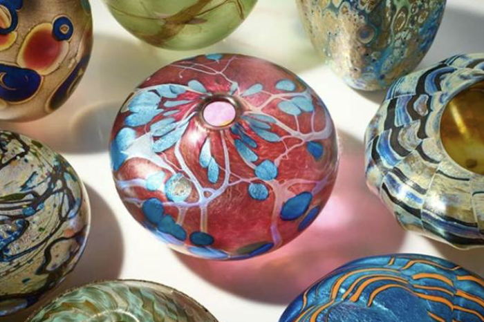Squat glass vases in bright colours with iridescent surfaces photographed from above and made by Peter Layton.