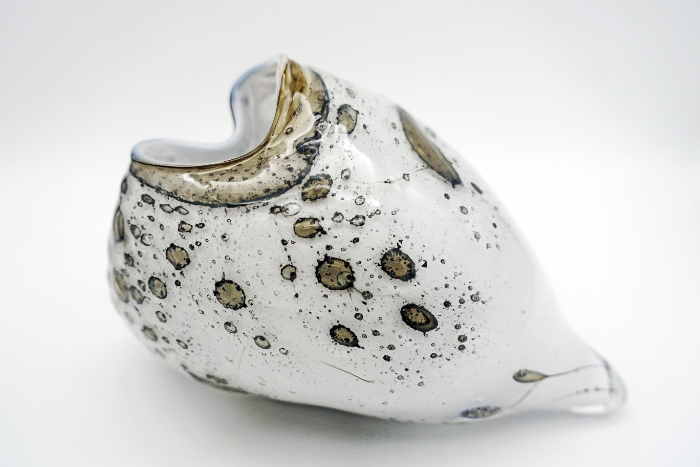 An organically shaped glass pollen sack made from white glass with honey infusions that creat brownish mottles to the surface.