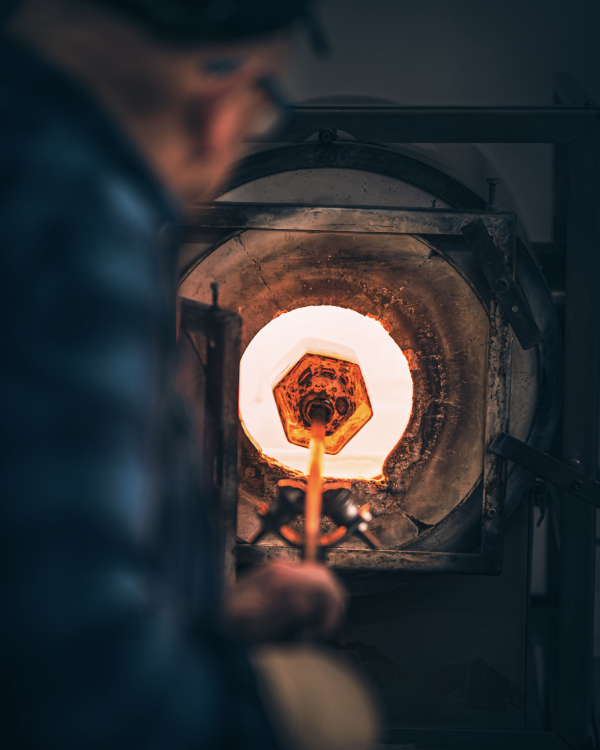 Mark Fenn warming hexagonal moulded glass in the glass furnace. View from behind his shoulder into the heat.