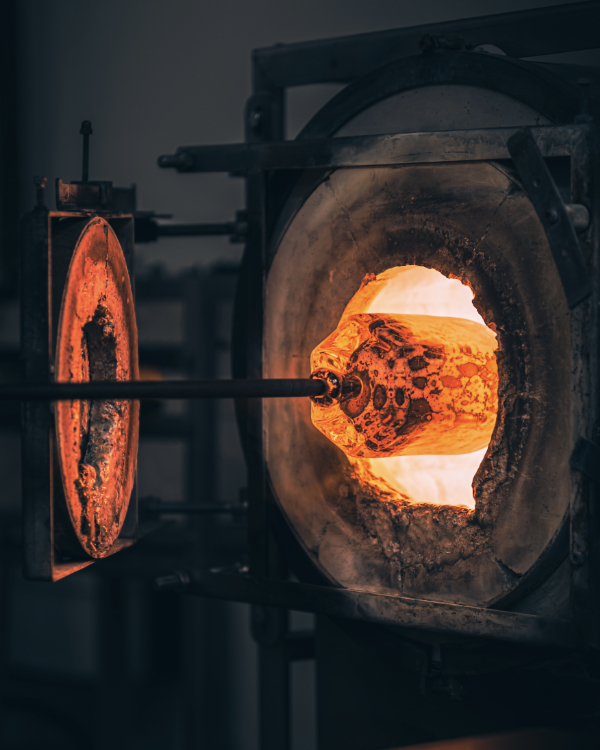 Side view of hexagonal vase made from molten glass entering the furnace for heating before hand-working with tools.