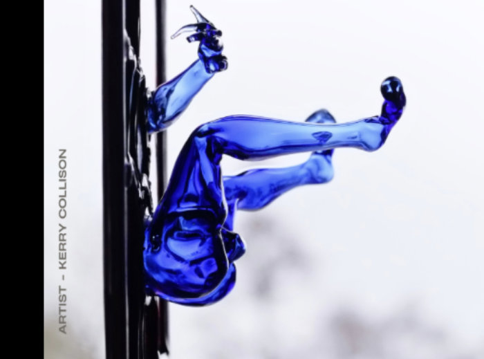 Detail of flame worked glass sculpture by Kerry Collison featuring arm, legs and bottom of a person jutting out from a flat panel, side view.