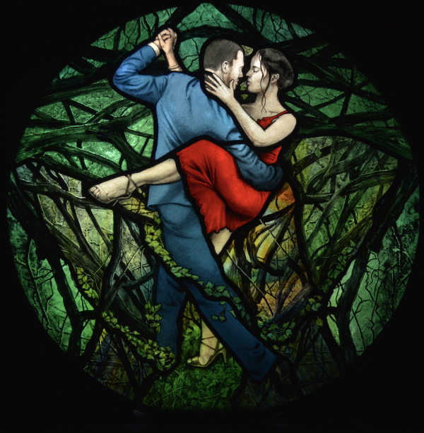 Rich dark green round stained glass panel painted with a couple dancing the tango with the woman in a red dress with her leg wrapped around the man in a blue suit as they are surrounded by tangled branches in a dark wood.