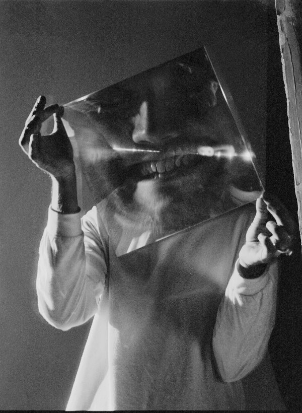 A person holding a sheet of glass in front of their face with a distorted face showing in the glass.