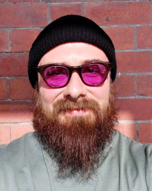 Head shot of Stacey Poultney wearing pink tint glasses and black beanie hat.