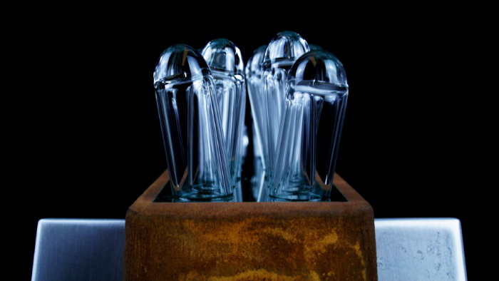 Glass and mixed media sculpture featuring clear glass tubes with round tops set at angles into wooded base.