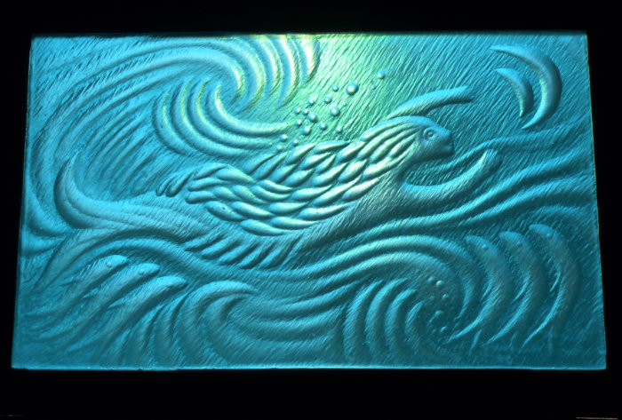 Aqua blue carved stained glass panel featuring a swimming creature by Jonathan Soper.