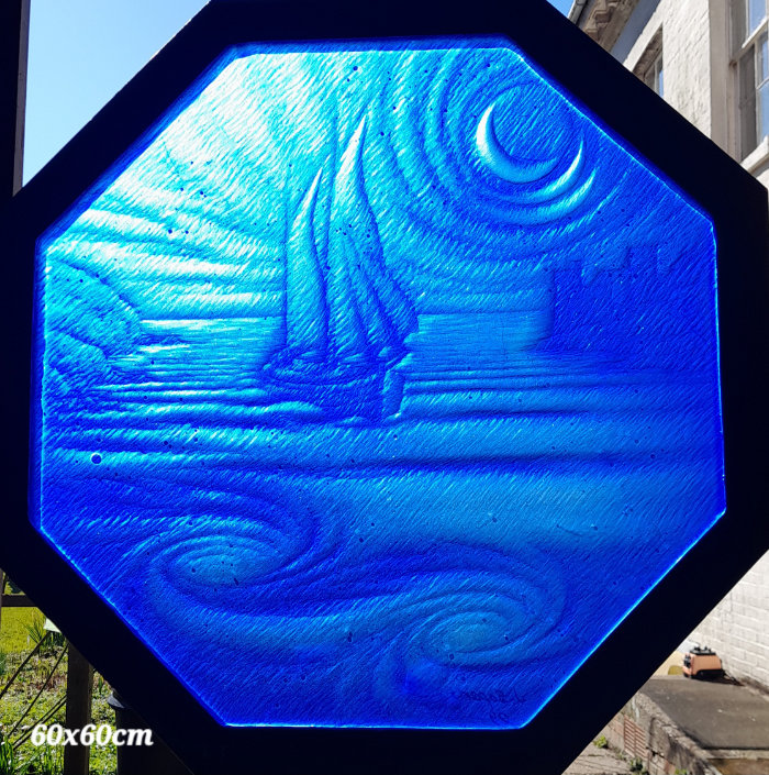 An octagonal black frame houses a rich blue scene of carved stained glass with a sailing boat travelling along a river by moonlight.