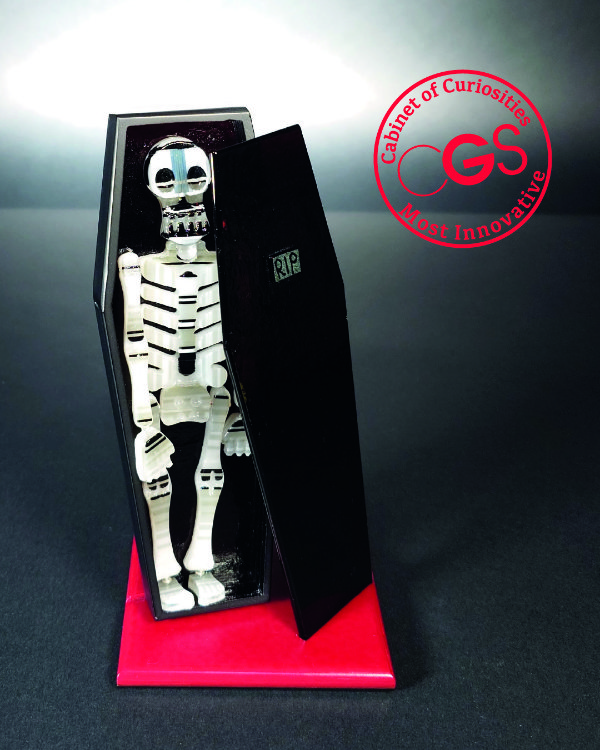 A kiln-formed black glass coffin and articulated white glass skeleton both standing upright with the lid balanced to the side to show the skeleton standing inside. By Ian Chadwick and called GlAsS Momento Mori.