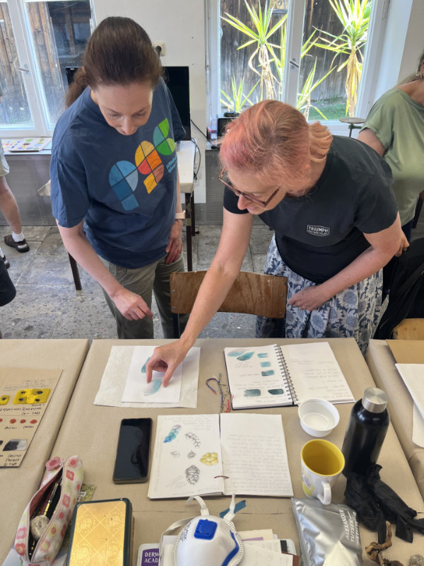 Tutor Tali Grinshpan stands next to Maria Donnai at the workbench examining glass samples and discussing the results.