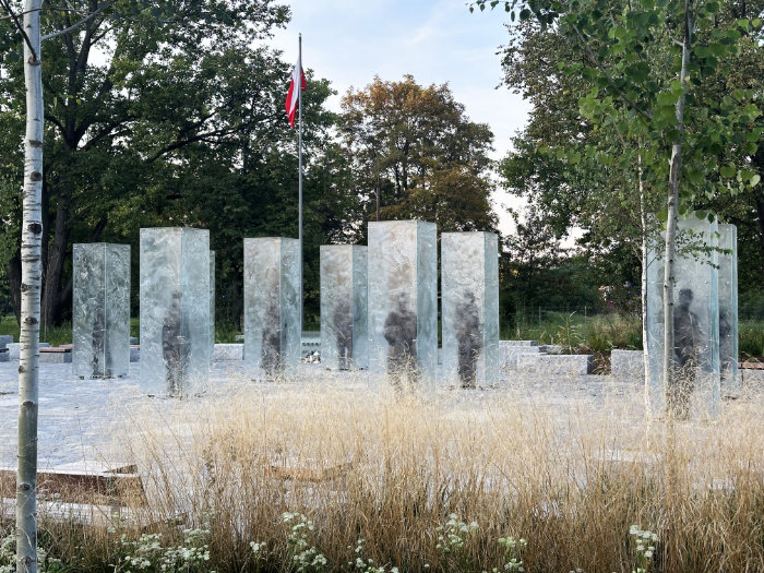 A view of the cuboids in daytime with grass in foreground and trees behind the sculptures.