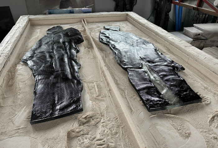 Two life-size cast and slumped glass partisans lie in a bed of sand in the studio.