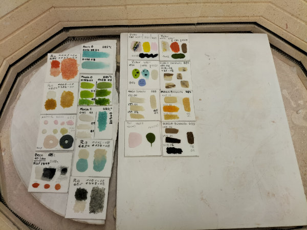 A view into a kiln with lots of small coloured samples laid out on the shelf.