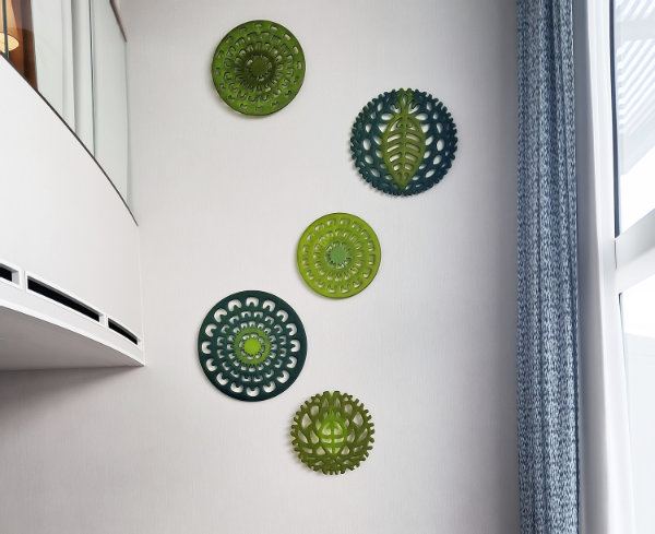 A view looking up to a white wall with five round glass patterned pieces arranged in organic formation. On the left is a mezzanine balcony and on the right a tall window with long curtain. Artwork called Flora Ascending, located in a Royal Caribbean luxury loft.