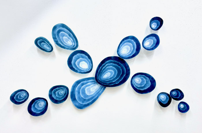 'Blue Ripples' kiln formed glass art wall installation featuring rounded organic shapes in tones of dark to light blue with concentric circles. Arranged with larger ones in the middle and smaller ones spreading out in a random arrangement.