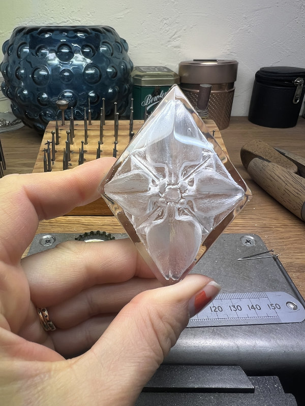 Close-up of hand holding a diamond-shaped piece of faceted glass to be used as a glass stone for a brooch setting.